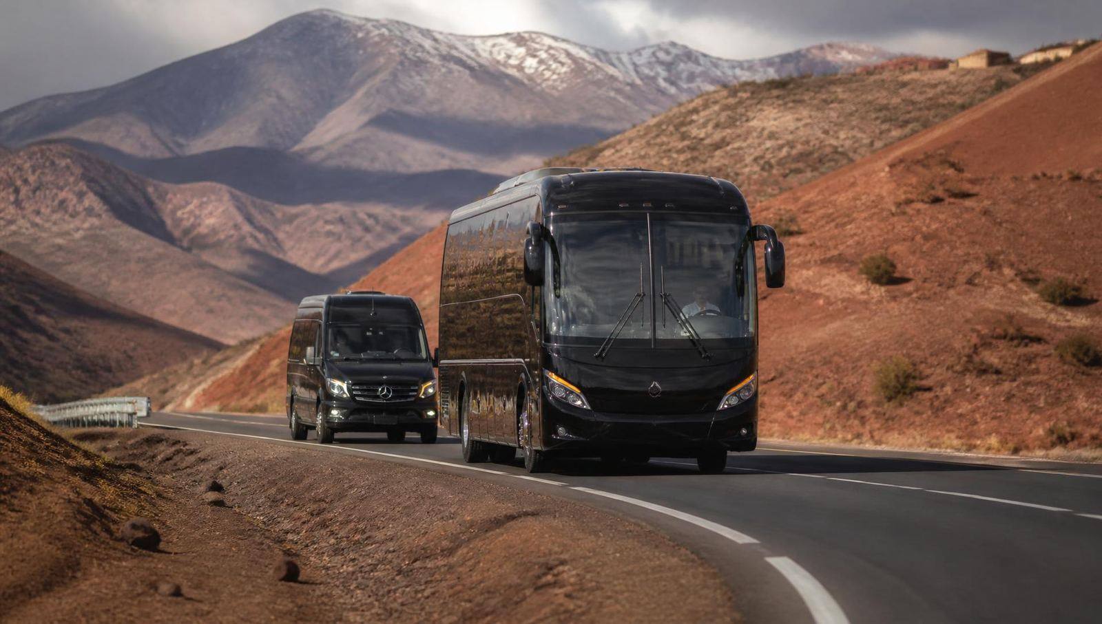 Black AMAZIR touring coach and Sprinter minibus driving in convoy on a High Atlas mountain road in Morocco